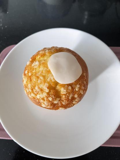 A M&S Lemon Drizzle Muffin with a course sugar and a bit of white icing on top. On a small white plate. 