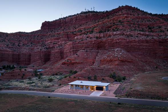 Drone shot of house at dawn nestled up against red cliffs in the background