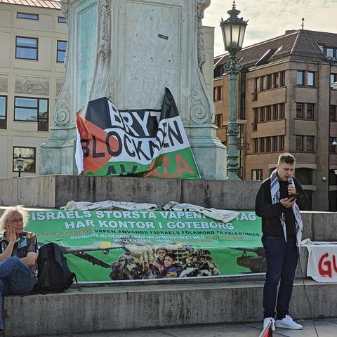 A banner saying "Break the blockade" in Swedish. A young man in black with a kufiya is standing to the right of it.