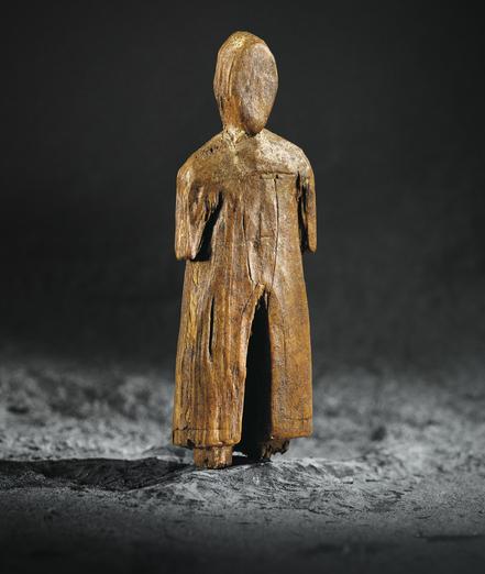 Figura humanoide de madera con sotana. En el abdomen tiene grabada una cruz.