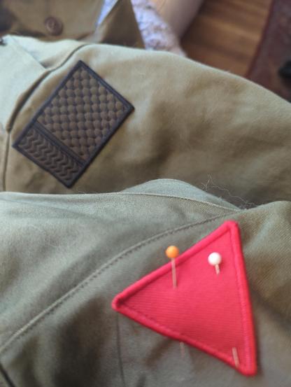 The sleeve of an olive drab M43 field jacket with a keffiyeh pattern patch on the shoulder and a straight-pinned red triangle patch in the foreground