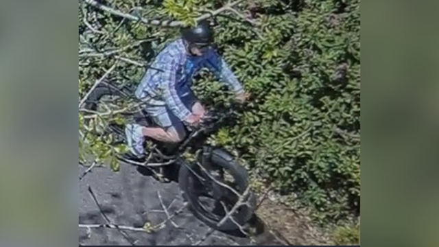 surveillance photo of a man on a bicycle wearing a blue plaid shirt