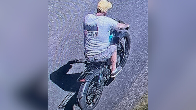 surveillance photo of a man in a yellow hat and a tshirt riding a black electric bike
