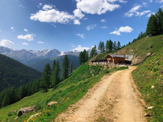 A trail in the mountains and a mountain hut. Snowy mountain peaks in the distance