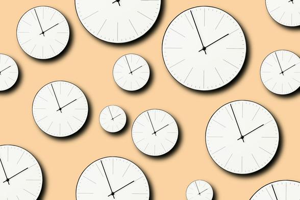 A beige wall filled with simple clocks 
