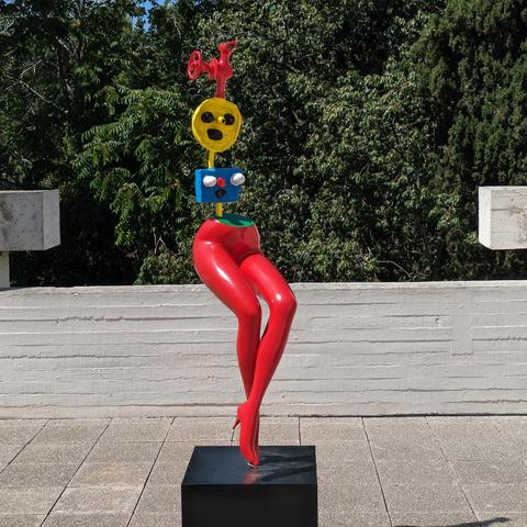 Outdoor statue with realistic red legs and high heels and a body and head made from geometric shapes (blue rectangle and yellow circle). 