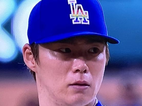 Close crop picture of Dodger pitcher Yamamoto rocking the blue hat with LA logo in rainbow colors. His eyes are deep concentration