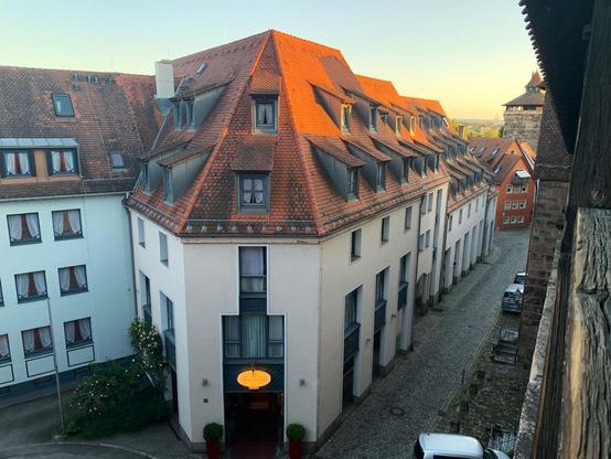Old style building in Nuremberg, steep sienna colored tiled roofs with two tiers of windows poking out from the roof. Three story white walls below. Viewed from a wooden walkway at about roof level.