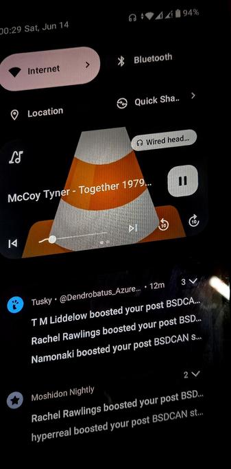  The photograph image shows a smartphone screen displaying a music player interface. The top of the screen shows the time as 00:29 on Saturday, June 14, with a battery level of 94%. The music player is playing a song titled "Together 1979" by McCoy Tyner, with a progress bar indicating the song is at 29 seconds. The playback controls include a pause button, a skip forward button, and a skip backward button. The music is being played through wired headphones, as indicated by the "Wired head..." label.

Below the music player, there is a section showing social media interactions. The post has been boosted by several users, including T M Liddelow, Rachel Rawlings, Namonaki, and Moshidon Nightly. The post contains the text "Tusk" and mentions "BSDCAN" and "BSDCAN." The post was made 12 minutes ago and has 3 comments and 2 likes. The background of the screen is dark, with the text and icons in white and light colors, providing a clear contrast.

 Ovis2-8B

🌱 Energy used: 0.263 Wh