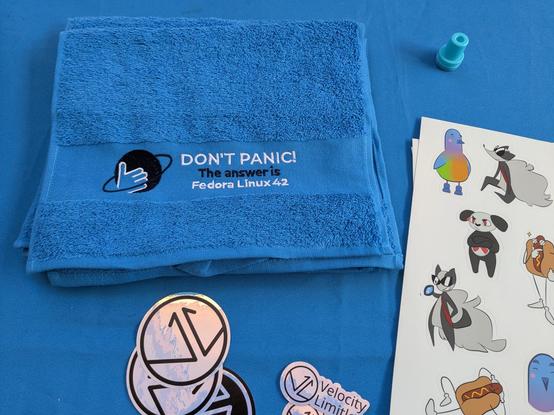 blue towel with the text "Don't Panic! The answer is Fedora Linux 42"