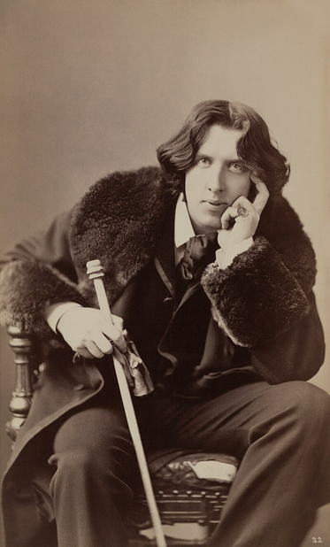 Oscar Wilde by Napoleon Sarony, albumen print on card mount, sheet 30.6 x 18.4 cm, on mount 33 x 19 cm. Notes 1045 U.S. Copyright Office. Title from item. No. 22. Copyright by N. Sarony. 

Oscar Wilde is captured in a full-length pose, leaning languidly to one side, his body curved with relaxed confidence.

He is dressed in fashionably eccentric attire: a velvet coat or jacket, silk cravat or ascot, knee breeches.

Wilde holds a cane.

His hair is shoulder-length.

https://en.wikipedia.org/wiki/Oscar_Wilde#/media/File:Oscar_Wilde_by_Napoleon_Sarony._Three-quarter-length_photograph,_seated.jpg