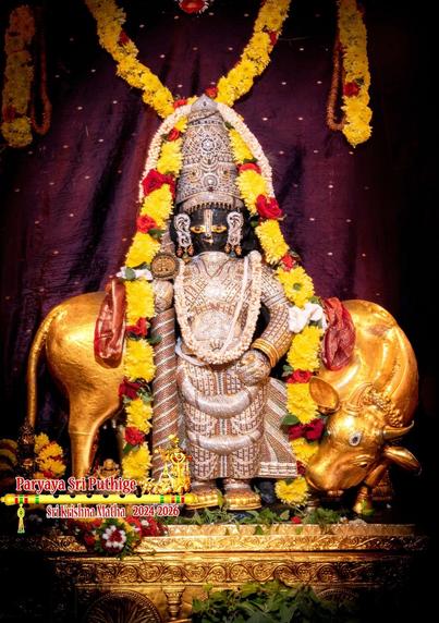 Idol of Hindu deity Krishna in diamond cladding, matching crown, holding a similarly-clad staff in right hand, left hand on left-front waist. Krishna stands in gold shoes on a gold perch with a gold cow behind him. Yellow flower garland (red roses in between) over the crown flowing all the way around either side of Krishna. Holy basil leaves at Krishna's feet.

A red shawl on the cow's back but only the two ends are visible (on either side of Krishna).

Maroon cloth (with sparse yellow spots) background. A string of yellow flowers hangs at the top over and behind Krishna.