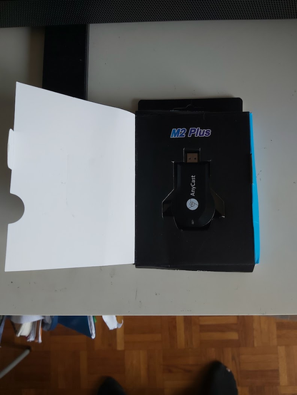 The M2 Plus anycast (streaming TV HDMI dongle) in its retail box, itself damaged by the worst-among-the-worst usual delivery guy while trying to insert this (and other more fragile stuff e.g. electronics parts) in my 1cm wide letterbox hole.