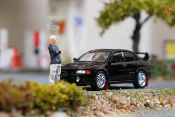 A Mitsubishi Lancer GSR Evolution V 1998 with Mud Flap, Pyrenees Black by Hobby Japan in 1:64 scale with 1:64 figure on AREA 164