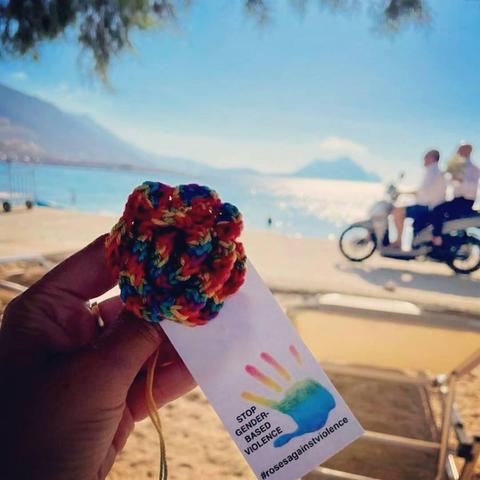 a knittet rose in rainbowcolers on a beach on amorgos, greece