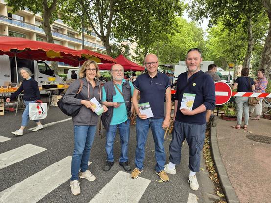 Quatre personnes devant l’entrée d’un marché avec des tracts dans la main.
