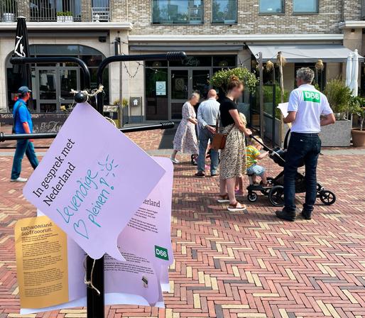 Foto van de straatactie van D66 de Bilt, met in de voorgrond de luisterboom en een D66-er in de achtergrond in gesprek met mensen