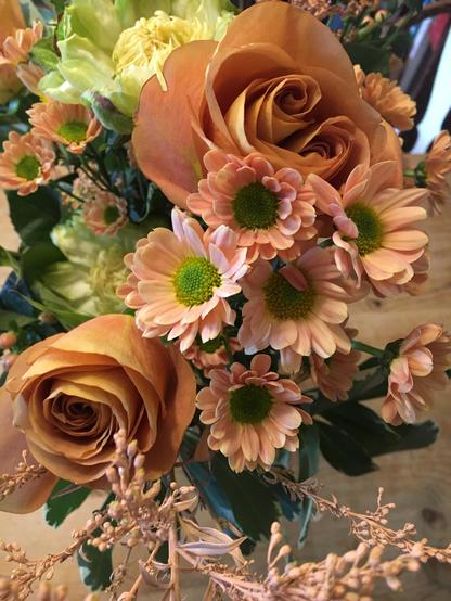 A vase filled with vibrant orange roses and fresh green daisies, creating a cheerful floral arrangement.