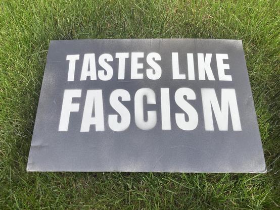 A piece of white foam core with black 3D printed letters placed on top of it which has been spray-painted and then the letters were removed.