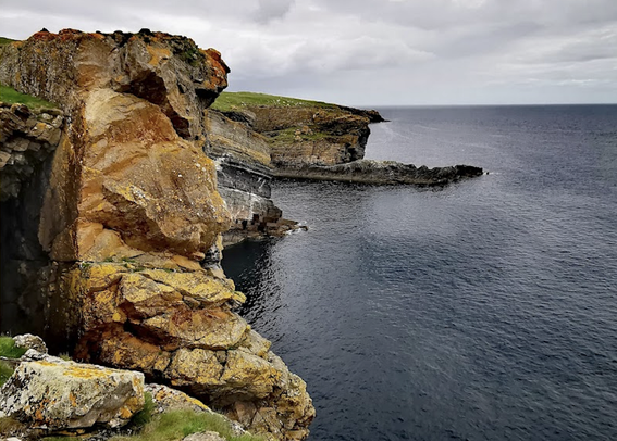Rust coloured rocks in the shape of a bear, looking out over the ocean, overcast sky. The bear has cute little ears and a turned up nose.