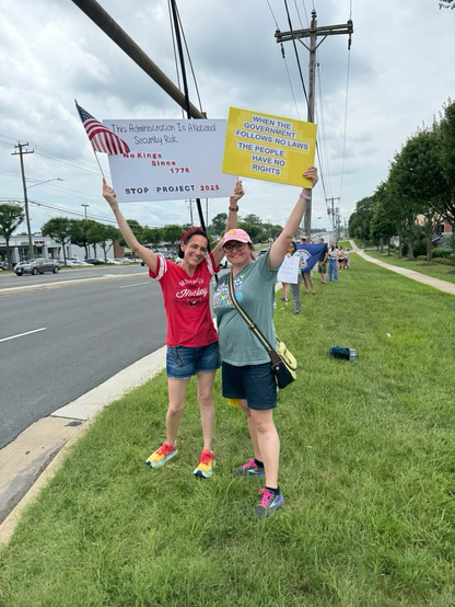Roadside protest with folks in the grass holding signs and smiling.