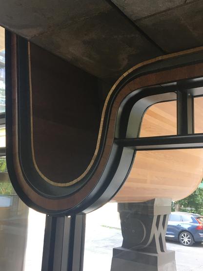 Curved wooden-framed window with a metal rail, showcasing a blend of natural and industrial design elements.