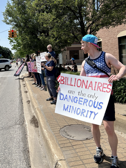 a guy in a stars & bars tank top holds a sign on a sidewalk:

BILLIONAIRES ARE THE ONLY DANGEROUS MINORITY 

h/t 
https://fediscience.org/@chasewnelson/114683403460330614