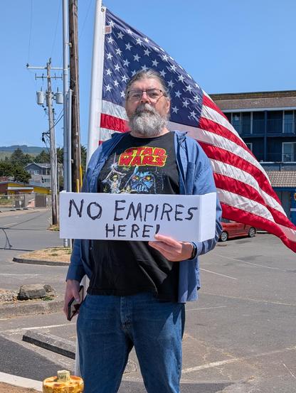 Me  wearing a classic Star Wars tee-shirt, standing in front of Old Glory, and holding a sign that reads "NO EMPIRES HERE!"