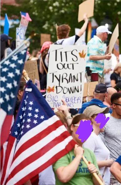 A sign is visible in the crowd at a protest in Alexandria, VA. The sign says "Tits Out - Tyrant Down - Sic Semper Tyrannis"