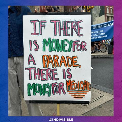 A protest sign reads "If there is money for a parade, there is money for medical" in colorful letters at a demonstration. The "Indivisible" logo is at the bottom right corner.