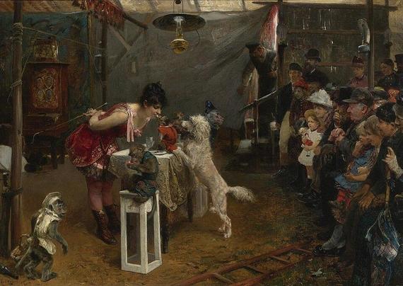 A circus scene of a woman in a pink frilly leotard taking a snack from a very little monkey on a table with performing dogs in the foreground and a watching Victorian crowd.