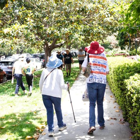 Two older women, one with a cane, the other with a patriotic shirt, walk away after attending rally