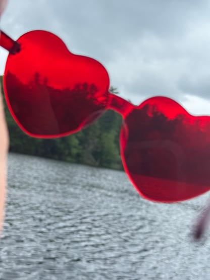 The view if the lake can be seen through bright  heart shaped sunglasses. 