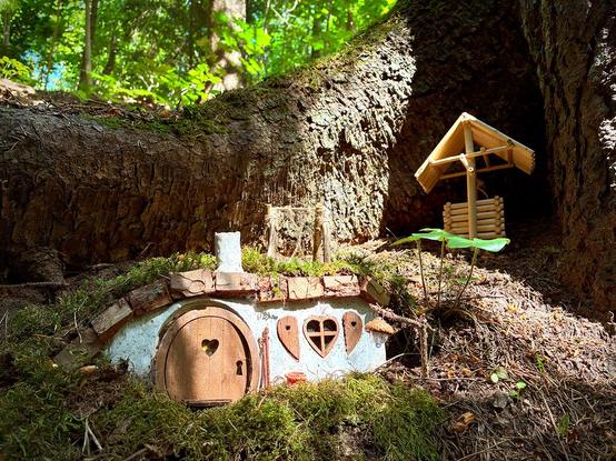 A miniature hobbit house in a forest, near an old tree root. 