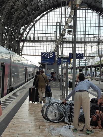 Photo of the train platform. On the left there is a tgv train stopped. On the platform some people disassemble their bikes and wrap them in plastic film