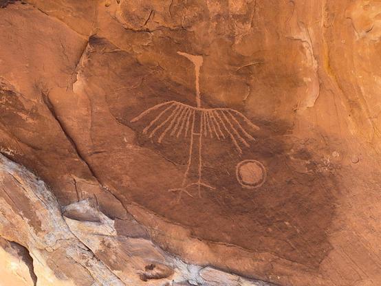Pecked figure on brown sandstone of a standing bird with its wings spread and a circle within a circle beside it.