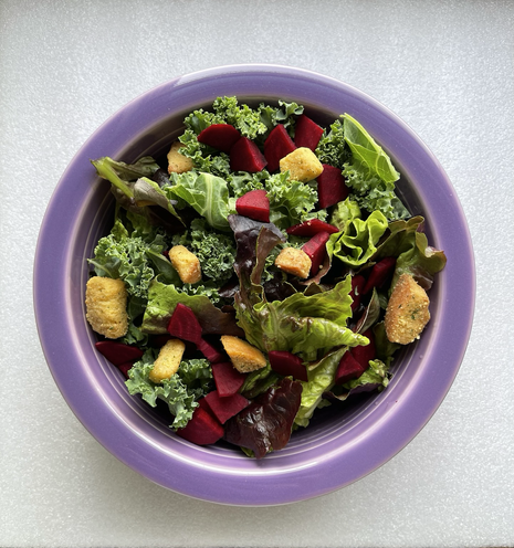 Salad in a purple bowl. You see croutons, leafy greens, and some diced up red beats.