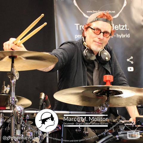 Der Drummer Marco M. Molitor schaut über sein Schlagzeug hinweg in die Kanera.