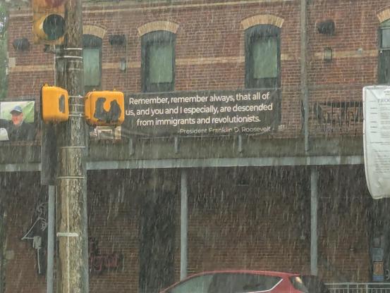A sign on a building in the rain that says "remember, remember always that all of us, and you and I especially, are descended from immigrants and revolutionists"
 President Franklin d. Roosevelt 
