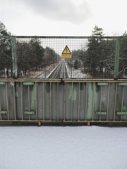 Blick auf zwei Bahngleise durch ein Gitter mit Warnschild.