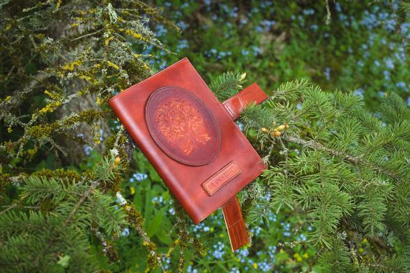 Light brown color leather notebook covers are set onto the pine branches. There is a hand carved oak tree on the decorative application. 