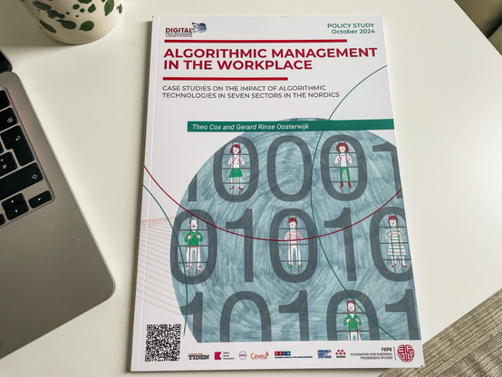 Picture of my desk, on the left a bit of my silver coloured notebook, in the back a large coffee mug with green dots, in the centre a printed publication titled Algorithmic management in the workplace, case studies on the impact of algorithmic technologies in seven sectors in the nordics, by Theo cox and Gerard rinse oosterwijk. 