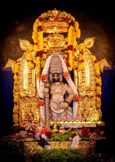 Idol of Hindu deity Krishna in diamond-studded cladding and a matching crown, holding a similarly clad staff in right hand, wearing gold shoes, standing on an ornate gold box. Holy basil leaves and assorted loose flowers at Krishna's feet. Also, a U-shaped dense string of white flowers hangs on the box. A similar thick string of flowers goes all around Krishna (over and behind his crown).

An extremely ornate gold arch with broad sides behind Krishna. The arch's sides depict a variety of animals and human (like) beings. Flags and flag-like objects stick out from behind the arch. A small gold umbrella is attached to the top (middle) of the arch. Strings of yellow flowers (with some red roses) hang from the umbrella and from the top of the arch.