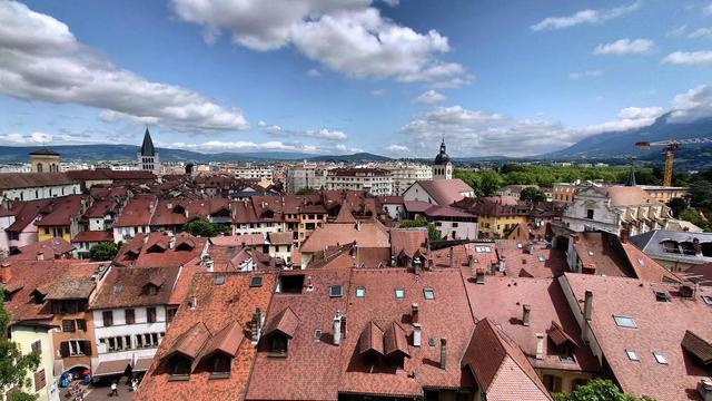 Blick über die roten Dächer von Annecy. Es sind auch 2 Kirchtürme zu sehen. Im Hintergrund die Alpen. Blauer Himmel mit ein paar Wolken. 