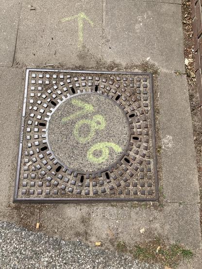 Round cover in a square frame, the number 186 is spray-painted on it