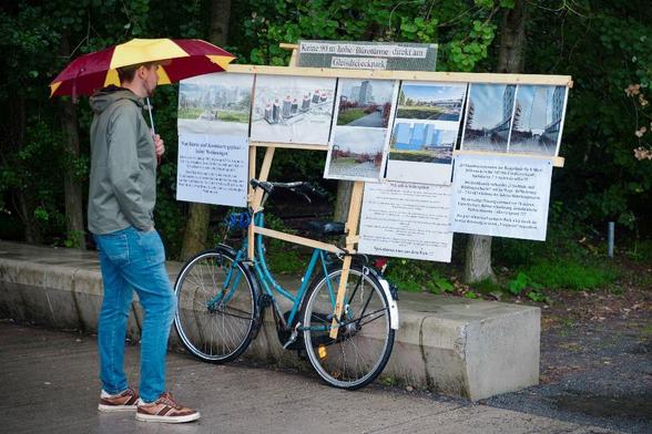 An einem abgestellten Fahrrad sind Infotafeln befestigt, ein Mann mit Regenschirm schaut sich dort an, was am Gleisdreieck geplant ist.