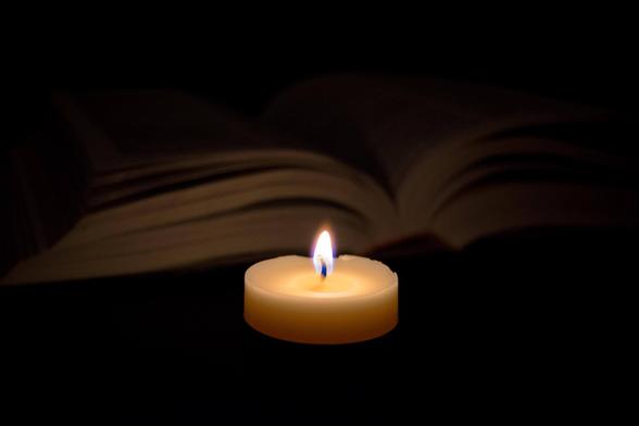 Una vela encendida ilumina de forma tenue un libro abierto que se encuentra justo detrás. 