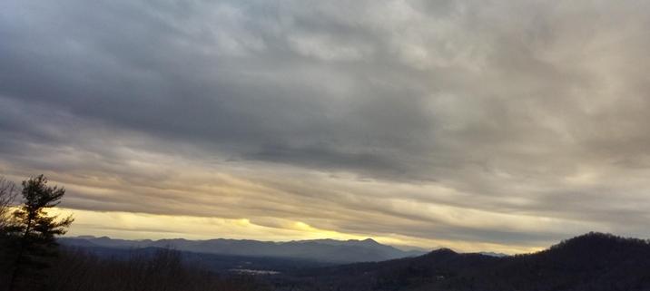 Sunset picture of mountains in the distance and clouds covering the sky with yellow towards the mountains