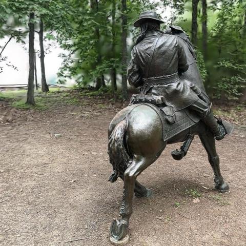 Statue of a solider wearing a hat and heavy coat riding a horse with (probably) a McClellan saddle turning a corner with the left front hoof held high