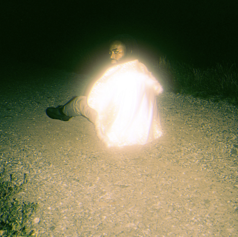 Chrisman with his back to the camera, sitting on the ground at night, wearing a highly reflective jacket.